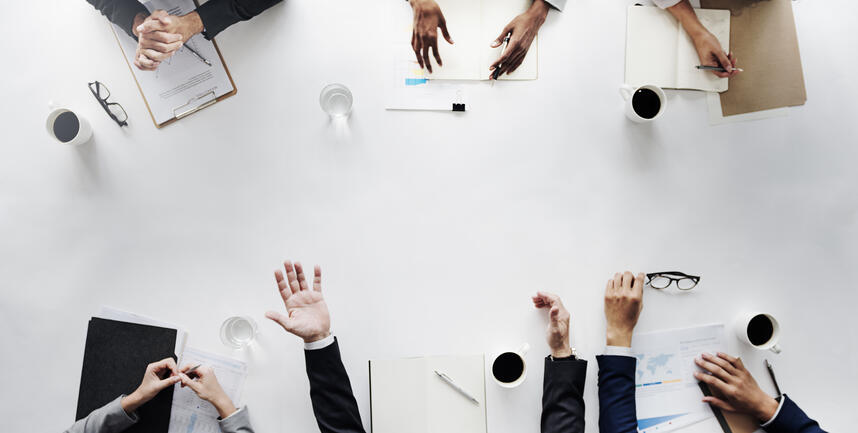 Hands of multiple businesspeople in suits sitting around a white table for meeting