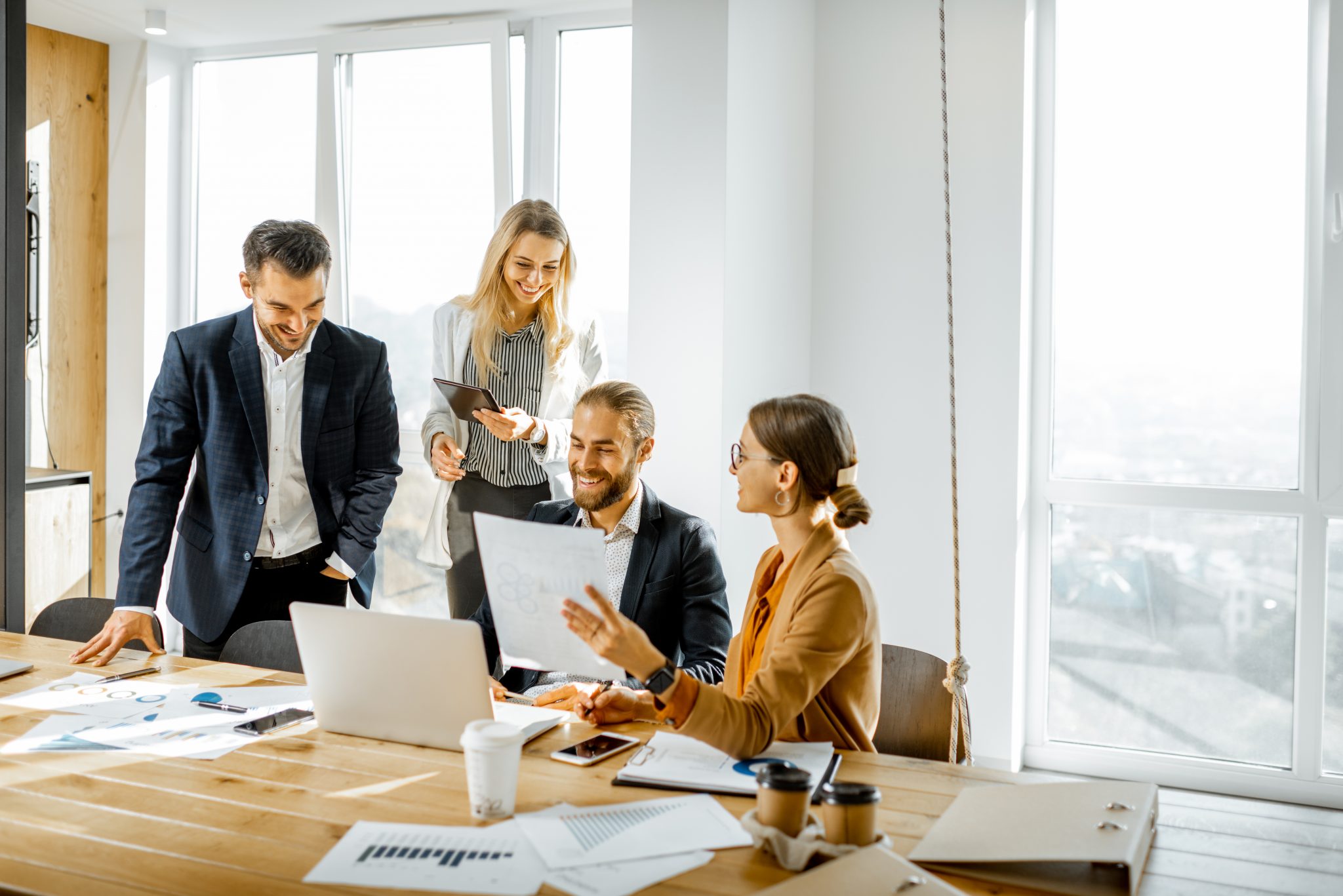 Group of a young office employees dressed casually in the suits having some office work at the large meeting table in the bright sunny room